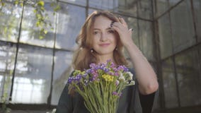 Portrait of pretty young woman holding bouquet of wild flowers standing at the old building looking at camera. Concept stock footage Portrait of pretty young woman holding bouquet of wild flowers standing at the old building looking at camera. Concept stock footage