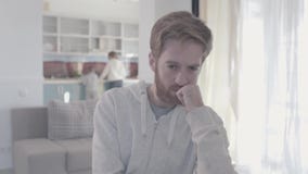 Portrait of sad bearded man standing in living room close up. Woman and boy are in the background. Family relationships