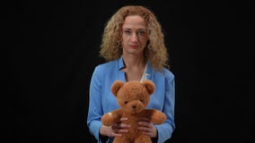 Portrait of serious Caucasian woman holding teddy bear looking at camera. Elegant lady posing with toy at black
