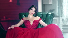 Portrait of sexy fashion woman in red evening glamour dress sitting on armchair looking at camera stock video Portrait of sexy fashion woman in red evening glamour dress sitting on armchair looking at camera stock video