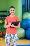 Portrait of smiling female fitness instructor writing in clipboard while standing in gym Royalty Free Stock Images Portrait of smiling female fitness instructor writing in clipboard while standing in gym Royalty Free Stock Images