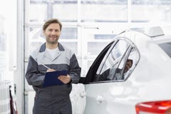 Portrait of smiling male automobile mechanic holding clipboard while standing by car in repair shop Royalty Free Stock Images Portrait of smiling male automobile mechanic holding clipboard while standing by car in repair shop Royalty Free Stock Images