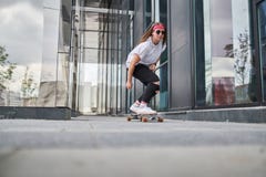 Portrait of sporty brunette riding skateboard on street among modern buildings