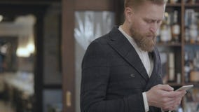 Portrait of a successful young bearded confident businessman typing on a cell phone while standing in a restaurant or an stock video Portrait of a successful young bearded confident businessman typing on a cell phone while standing in a restaurant or an stock video