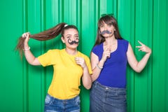 Young women holding photo boot props against green metal wall background. Party concept.