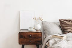 Portrait white frame mockup on retro wooden bedside table. Modern white ceramic vase with dry Lagurus ovatus grass and