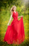 Portrait of young beautiful blonde woman wearing a long red elegant dress posing in a green meadow. Fashionable attractive royalty free stock image Portrait of young beautiful blonde woman wearing a long red elegant dress posing in a green meadow. Fashionable attractive royalty free stock image