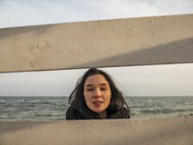 Portrait of a young girl with brown hairs view through a wooden fence on the background of the sea royalty free stock image Portrait of a young girl with brown hairs view through a wooden fence on the background of the sea royalty free stock image
