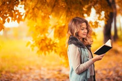 Portrait of a young girl in fur vest and reading book on background autumn park stock photo Portrait of a young girl in fur vest and reading book on background autumn park stock photo
