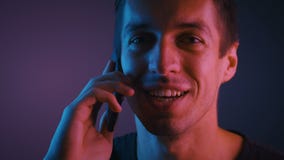 Portrait of a young man talking on a cell phone in a room lit by a neon light stock video footage Portrait of a young man talking on a cell phone in a room lit by a neon light stock video footage
