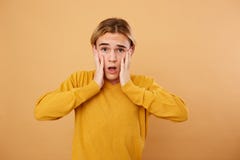 Portrait of young surprised blond guy dressed in yellow sweater is posing in the studio on the beige background stock images Portrait of young surprised blond guy dressed in yellow sweater is posing in the studio on the beige background stock images