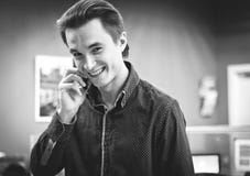 Portret młody uśmiechnięty facet opowiada na telefonie komórkowym w koszula w biurowym środowisku, czarny i biały wizerunek zdjęcia royalty free Portret młody uśmiechnięty facet opowiada na telefonie komórkowym w koszula w biurowym środowisku, czarny i biały wizerunek zdjęcia royalty free