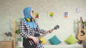 Portret rozochocona muzułmańska młoda kobieta w hijab bawić się gitarę elektryczną w domu zdjęcie wideo Portret rozochocona muzułmańska młoda kobieta w hijab bawić się gitarę elektryczną w domu zdjęcie wideo