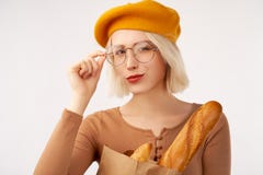Portret szczęśliwa uśmiechnięta kobieta trzyma papierową torbę z długim białego chleba baguette, będący ubranym żółtego beret i s obrazy stock Portret szczęśliwa uśmiechnięta kobieta trzyma papierową torbę z długim białego chleba baguette, będący ubranym żółtego beret i s obrazy stock