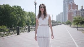 Portret urocza młoda dziewczyna jest ubranym okulary przeciwsłonecznych i długiego białego lato mody sukni odprowadzenia puszek z zbiory wideo Portret urocza młoda dziewczyna jest ubranym okulary przeciwsłonecznych i długiego białego lato mody sukni odprowadzenia puszek z zbiory wideo