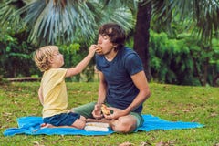 Portret van een jonge vader en zijn zoon die van een hamburger in een park en het glimlachen genieten royalty-vrije stock fotografie Portret van een jonge vader en zijn zoon die van een hamburger in een park en het glimlachen genieten royalty-vrije stock fotografie