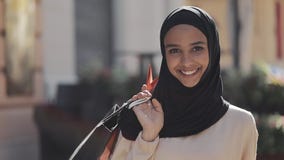 Portret van gelukkige jonge moslimvrouw die in hijab de straat met het winkelen zakken in haar hand terugtrekken zich Online Wink stock video Portret van gelukkige jonge moslimvrouw die in hijab de straat met het winkelen zakken in haar hand terugtrekken zich Online Wink stock video