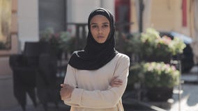 Portret van het mooie jonge Moslimvrouw dragen die hijab headscarf de camera onderzoeken die met gekruiste handen zich bevinden stock footage Portret van het mooie jonge Moslimvrouw dragen die hijab headscarf de camera onderzoeken die met gekruiste handen zich bevinden stock footage