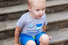 Portret van mooie babyjongen buiten Het aanbiddelijke jonge geitje bekijkt met rente iets die op de trede zitten royalty-vrije stock foto's Portret van mooie babyjongen buiten Het aanbiddelijke jonge geitje bekijkt met rente iets die op de trede zitten royalty-vrije stock foto's