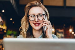 Portretonderneemster die in glazen in koffie voor laptop zitten, die op telefoon spreken Het meisje blogger communiceert telefoni stock foto Portretonderneemster die in glazen in koffie voor laptop zitten, die op telefoon spreken Het meisje blogger communiceert telefoni stock foto