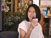 Portretten die van Aziatische vrouw een kop van koffie houden die rechts aan haar kijken in comfortabele koffiewinkel royalty-vrije stock fotografie Portretten die van Aziatische vrouw een kop van koffie houden die rechts aan haar kijken in comfortabele koffiewinkel royalty-vrije stock fotografie