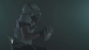 Porträt des bärtigen Spielers des amerikanischen Fußballs im Sturzhelmanfang, der, einen Schlag auf dem dunklen Hintergrund mache stock video footage Porträt des bärtigen Spielers des amerikanischen Fußballs im Sturzhelmanfang, der, einen Schlag auf dem dunklen Hintergrund mache stock video footage