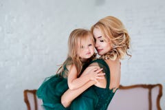 Porträt einer schönen jungen Mutter mit einer netten blonden Tochter, die im weißen Innenraum sitzt, kleidete im eleganten Grün a stockfoto Porträt einer schönen jungen Mutter mit einer netten blonden Tochter, die im weißen Innenraum sitzt, kleidete im eleganten Grün a stockfoto