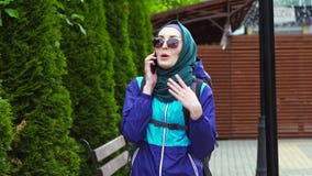 Porträt eines Mädchentouristen in einem Kopftuch und der Sonnenbrille mit einem Rucksack sprechend am Telefon Porträt eines Mädchentouristen in einem Kopftuch und der Sonnenbrille mit einem Rucksack sprechend am Telefon