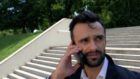 Porträt eines stilvollen und attraktiven jungen Mannes mit einem Bart, lächelnd und sprechen am Telefon im Park an einem sonnigen stock video Porträt eines stilvollen und attraktiven jungen Mannes mit einem Bart, lächelnd und sprechen am Telefon im Park an einem sonnigen stock video