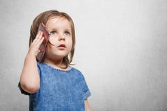 Porträt ot attraktives kleines Kind mit durchdachtem Blick, hält modernen Handy in den Händen, macht ihrer Mutter Anruf, trägt de Stockbild Porträt ot attraktives kleines Kind mit durchdachtem Blick, hält modernen Handy in den Händen, macht ihrer Mutter Anruf, trägt de Stockbild
