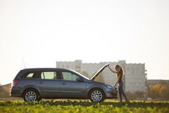 Posi??o atrativa nova da mulher no carro de prata que olha sob a capa estalada no fundo claro do espa?o da c?pia do c?u Transport imagem de stock Posi??o atrativa nova da mulher no carro de prata que olha sob a capa estalada no fundo claro do espa?o da c?pia do c?u Transport imagem de stock