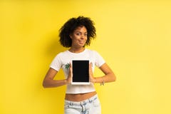 Position afro-américaine assez jeune de femme et tablette d'utilisation d'isolement au-dessus du fond jaune photos stock Position afro-américaine assez jeune de femme et tablette d'utilisation d'isolement au-dessus du fond jaune photos stock