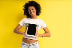 Position afro-américaine assez jeune de femme et tablette d'utilisation d'isolement au-dessus du fond jaune photos libres de droits Position afro-américaine assez jeune de femme et tablette d'utilisation d'isolement au-dessus du fond jaune photos libres de droits