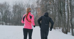 Positive beautiful young healthy couple running with sportswear through the forest in the winter morning stock video footage Positive beautiful young healthy couple running with sportswear through the forest in the winter morning stock video footage