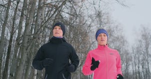 Positive beautiful young healthy couple running with sportswear through the forest in the winter morning stock footage Positive beautiful young healthy couple running with sportswear through the forest in the winter morning stock footage