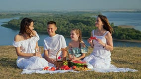 Positive lady with daughters and son on riverbank at picnic