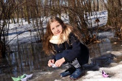 A little girl playing with paper boats in early spring semi-frozen puddles stock images A little girl playing with paper boats in early spring semi-frozen puddles stock images