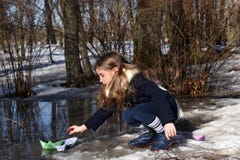 A little girl playing with paper boats in early spring semi-frozen puddles royalty free stock image A little girl playing with paper boats in early spring semi-frozen puddles royalty free stock image