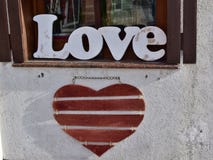 Posição de madeira ‘do amor ‘da palavra na soleira e no coração de madeira vermelho que penduram na parede na rua da cidade fotografia de stock Posição de madeira ‘do amor ‘da palavra na soleira e no coração de madeira vermelho que penduram na parede na rua da cidade fotografia de stock