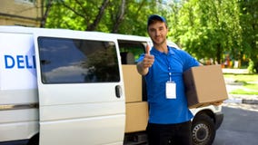 Postal office worker taking parcel box from delivery van and showing thumbs up stock photo Postal office worker taking parcel box from delivery van and showing thumbs up stock photo