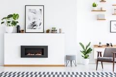 Poster and plant on white board with fireplace in cosy living room interior with armchair. Real photo stock image Poster and plant on white board with fireplace in cosy living room interior with armchair. Real photo stock image