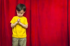Praying Mixed Race Boy In Front Of Red Curtain Stock Image