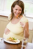 Pregnant woman in kitchen eating chicken