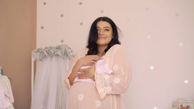 Pregnant woman looking on clothes in a tender future baby room. 4k