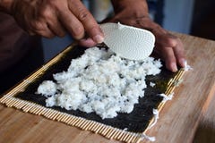 Preparando i sushi casalinghi mettendo riso bianco su uno strato di alga secco di nori sulla stuoia di bambù immagini stock libere da diritti Preparando i sushi casalinghi mettendo riso bianco su uno strato di alga secco di nori sulla stuoia di bambù immagini stock libere da diritti