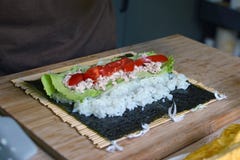 Preparazione dei sushi casalinghi con riso bianco, il tonno, i pomodori e l'insalata su uno strato di alga secco di nori sulla st fotografia stock libera da diritti Preparazione dei sushi casalinghi con riso bianco, il tonno, i pomodori e l'insalata su uno strato di alga secco di nori sulla st fotografia stock libera da diritti