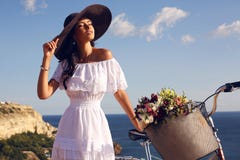 Pretty brunette in elegant dress and hat riding a bicycle along the coast stock photos Pretty brunette in elegant dress and hat riding a bicycle along the coast stock photos