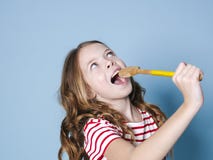 Pretty cool and young girl uses cooking spoon as microphone and sings in front of blue background and is having a lot of fun