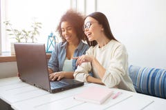 Pretty girls are sitting at the table and chatting on the laptop. They are sitting near window. Afro american girl is Stock Photography Pretty girls are sitting at the table and chatting on the laptop. They are sitting near window. Afro american girl is Stock Photography