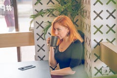 Pretty happy redheaded caucasian woman in black shirt drinks cup of coffee in the modern cafe alone stock photo Pretty happy redheaded caucasian woman in black shirt drinks cup of coffee in the modern cafe alone stock photo
